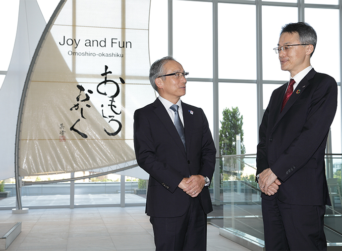 At the entrance to HORIBA BIWAKO E-HARBOR, HORIBA's research and development and production center. <br>The phrase “Omoshiro Okashiku,” written on the sail, was handwritten by the founder, Masao Horiba.